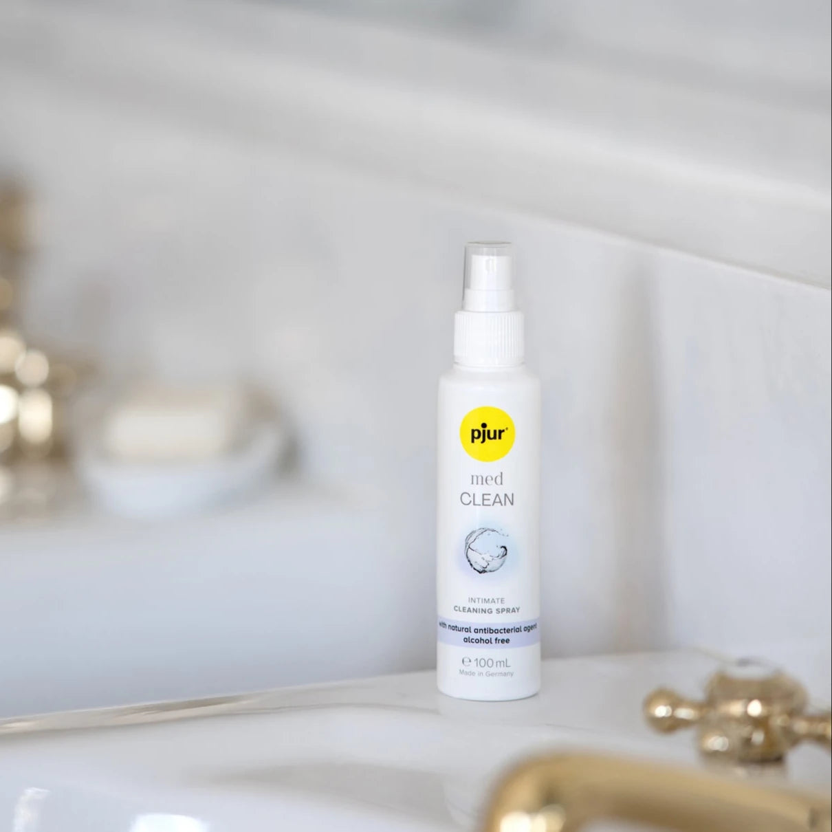 Pjur Med Clean Spray stående ved håndvask i lyst badeværelse – en alkohol- og parfumefri intimrens, der skånsomt fjerner bakterier og forlænger levetiden på sexlegetøj og hudvenlige produkter fra Nevola.