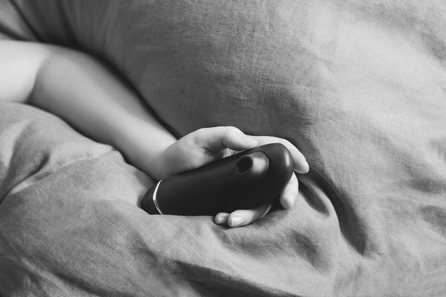 Kvinde ligger under et tæppe med en Womanizer lufttryksvibrator i hånden; stemningsfuldt billede til kollektionen vibratorer til kvinder hos Nevola, der rummer eksklusive modeller som Womanizer og Lovense Lush 4 til sanselig nydelse.