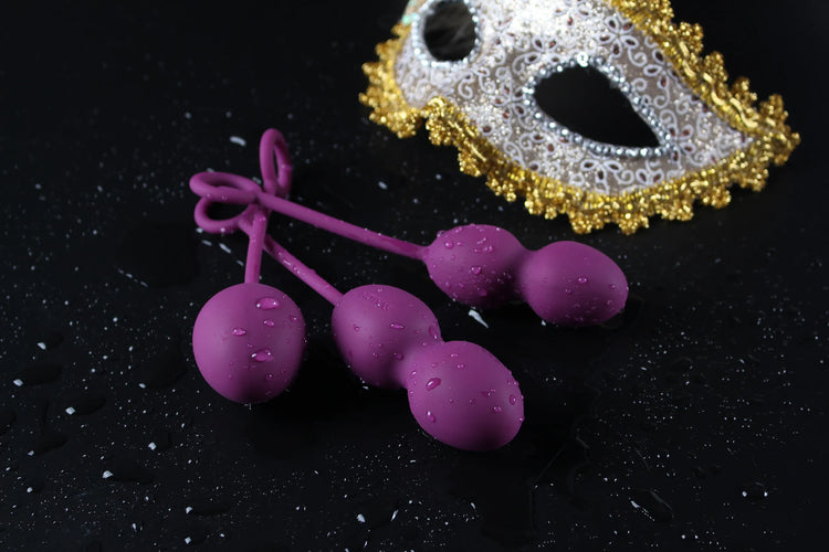 Svakom bækkenbundskugler i lilla silikone med vanddråber på sort baggrund ved siden af en dekorativ maske; symbol på elegance og nydelse i Svakom kollektionen hos Nevola, hvor teknologi møder sanselig træning.