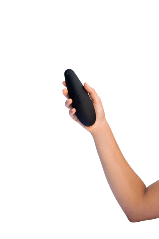 Hånd der holder en Womanizer Classic 2 lufttryksvibrator i sort. Produktet vises tæt for at fremhæve det ergonomiske design, de enkle knapper og den blide, kontaktløse stimulering til rolig nydelse.