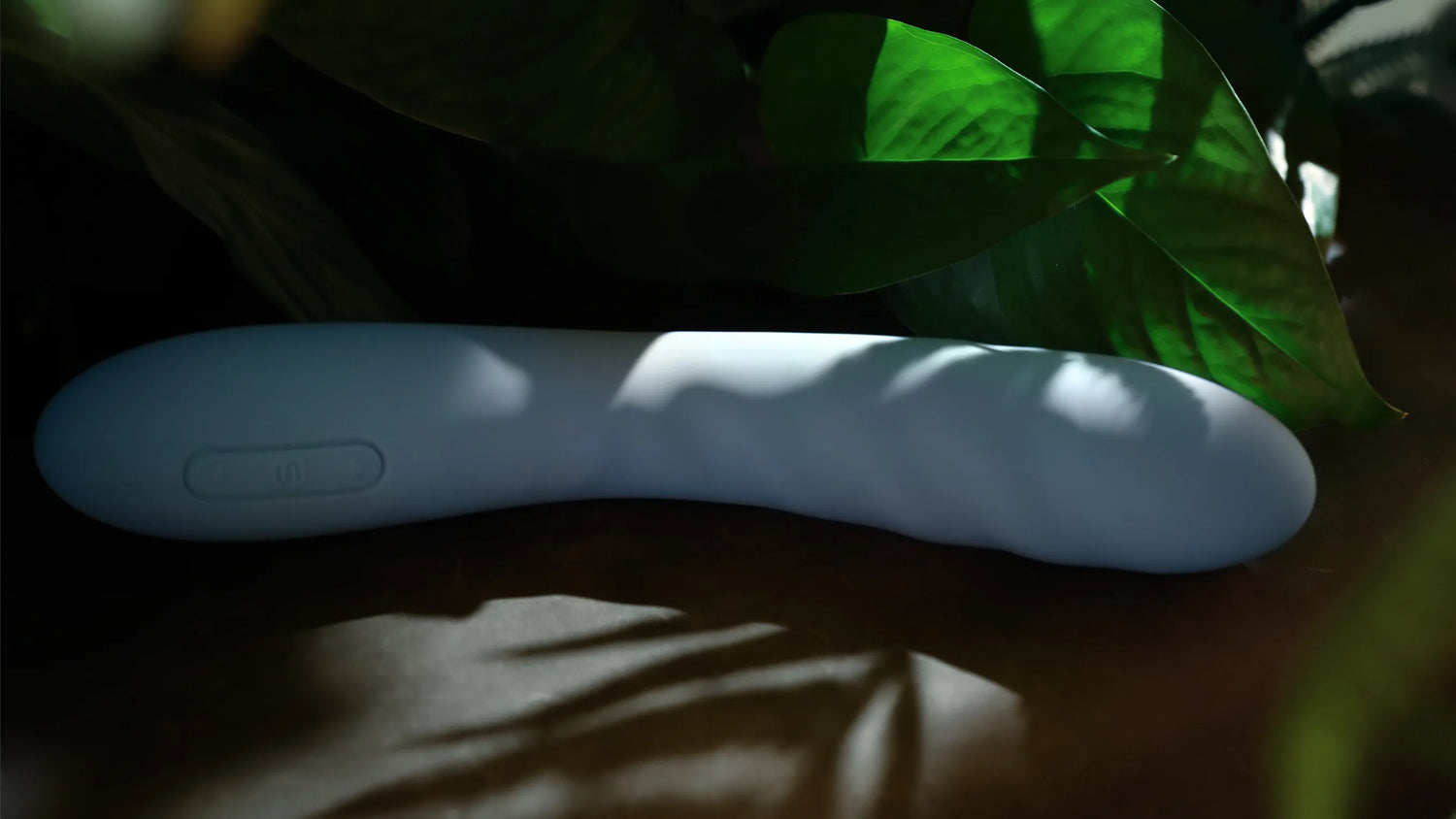 Ava Neo vibrator i blå silikone placeret blandt grønne blade og bløde skygger. Intimproduktet forener natur og sanselig wellness, skabt til moderne kvinder, der ønsker diskret nydelse i et æstetisk og stilfuldt design.