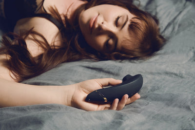 Afslappet kvinde hviler med Womanizer Premium 2 i hånden – et stilfuldt og diskret intimprodukt til dyb nydelse. Sensuel stemning skabt af Nevola med levering i hele Danmark.