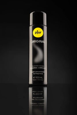 Pjur Original glidecreme 100 ml fotograferet på sort baggrund med elegant refleksion. Premium silikonebaseret smøremiddel, kendt for koncentreret effekt, neutral duft og sikker anvendelse i intim wellness og erotik.