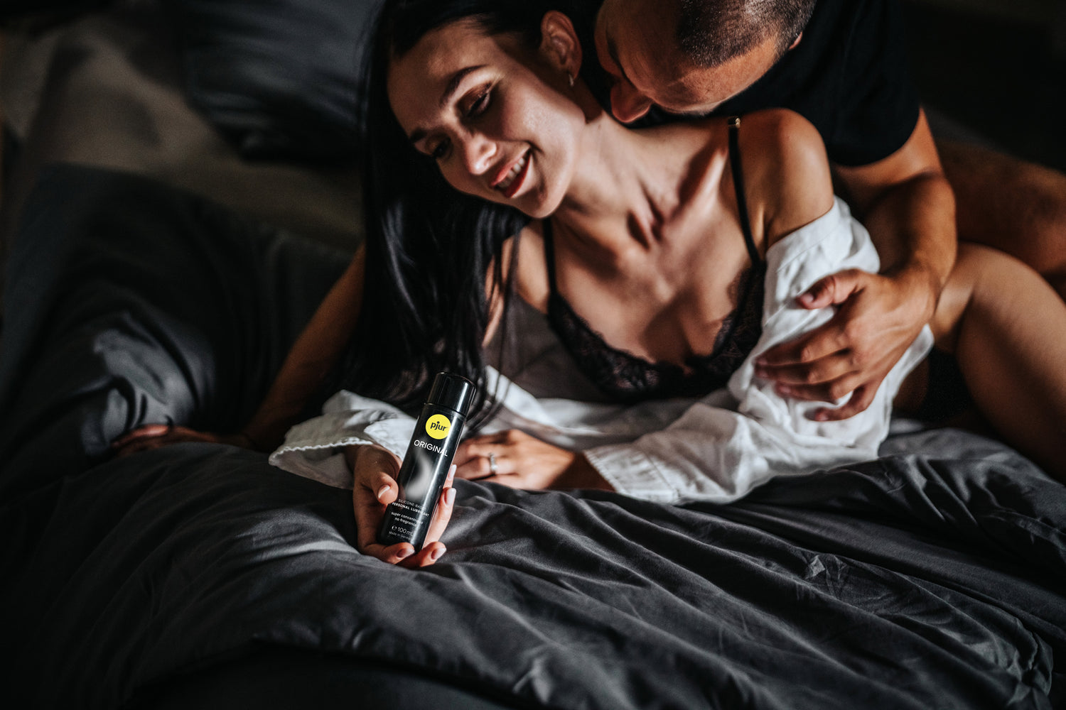 Kvinde i sensuel stemning holder Pjur Original glidecreme 100 ml under intime øjeblikke i sengen. Skaber blød og langvarig glid, ideel til sexlegetøj og parforholdets nydelse.