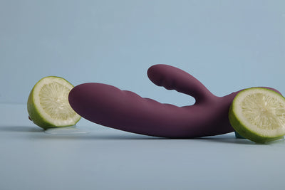 Elegant lilla rabbit vibrator med dobbeltsidig stimulation placeret kunstnerisk ved friske limefrugter. Intimproduktet er designet til sanselig nydelse, diskret brug og moderne wellness – perfekt til kvinder, der søger dyb og blid stimulering.