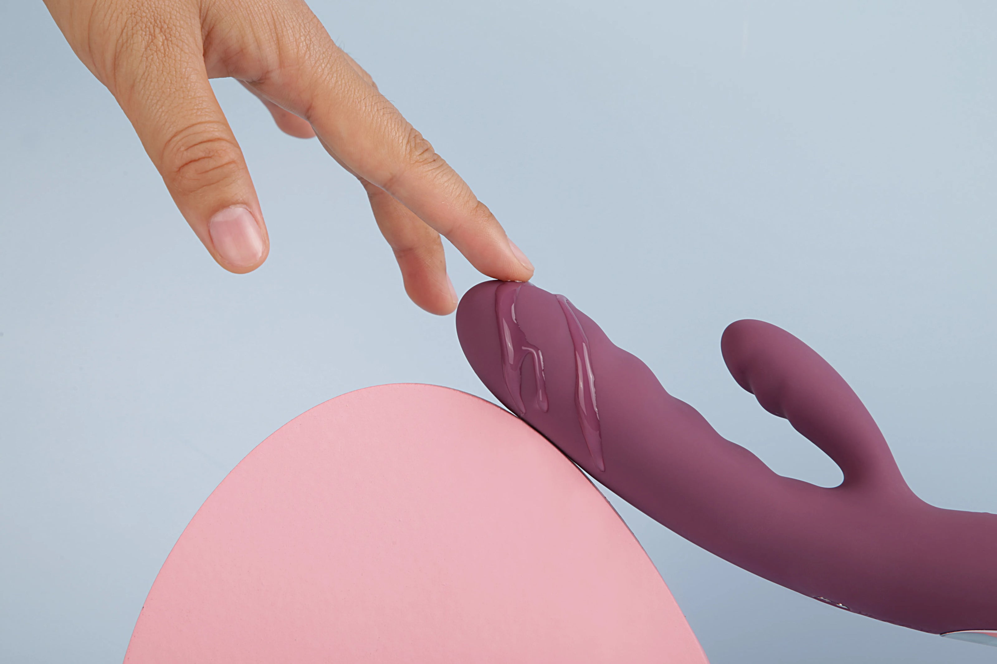 Lilla rabbit vibrator med blød silikoneoverflade, illustreret med glidecreme og kvindens hånd, der rører produktet. Intimprodukt designet til dobbeltstimulation, sanselig wellness og diskret nydelse i intime øjeblikke.