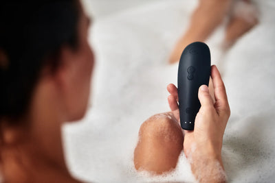 Womanizer Classic 2 lufttryksvibrator i sort holdt af kvinde med skum i hånden under bad. Vandtæt sexlegetøj til kvinder, ideelt til intime wellness-oplevelser i brusebad og kar.