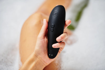 Womanizer Classic 2 lufttryksvibrator i sort i kvindes hånd, omgivet af skumbad. Elegant sexlegetøj med intuitiv styring og Pleasure Air-teknologi til sanselige øjeblikke og diskret nydelse.