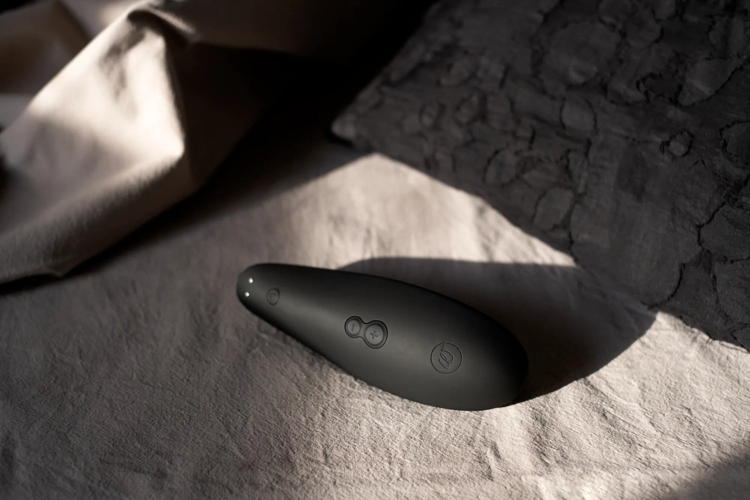 Womanizer Classic 2 lufttryksvibrator i sort placeret på seng med blødt stof. Elegant sexlegetøj til kvinder med Pleasure Air-teknologi, vandtæt design og diskret udformning til sanselig nydelse i hverdagen.