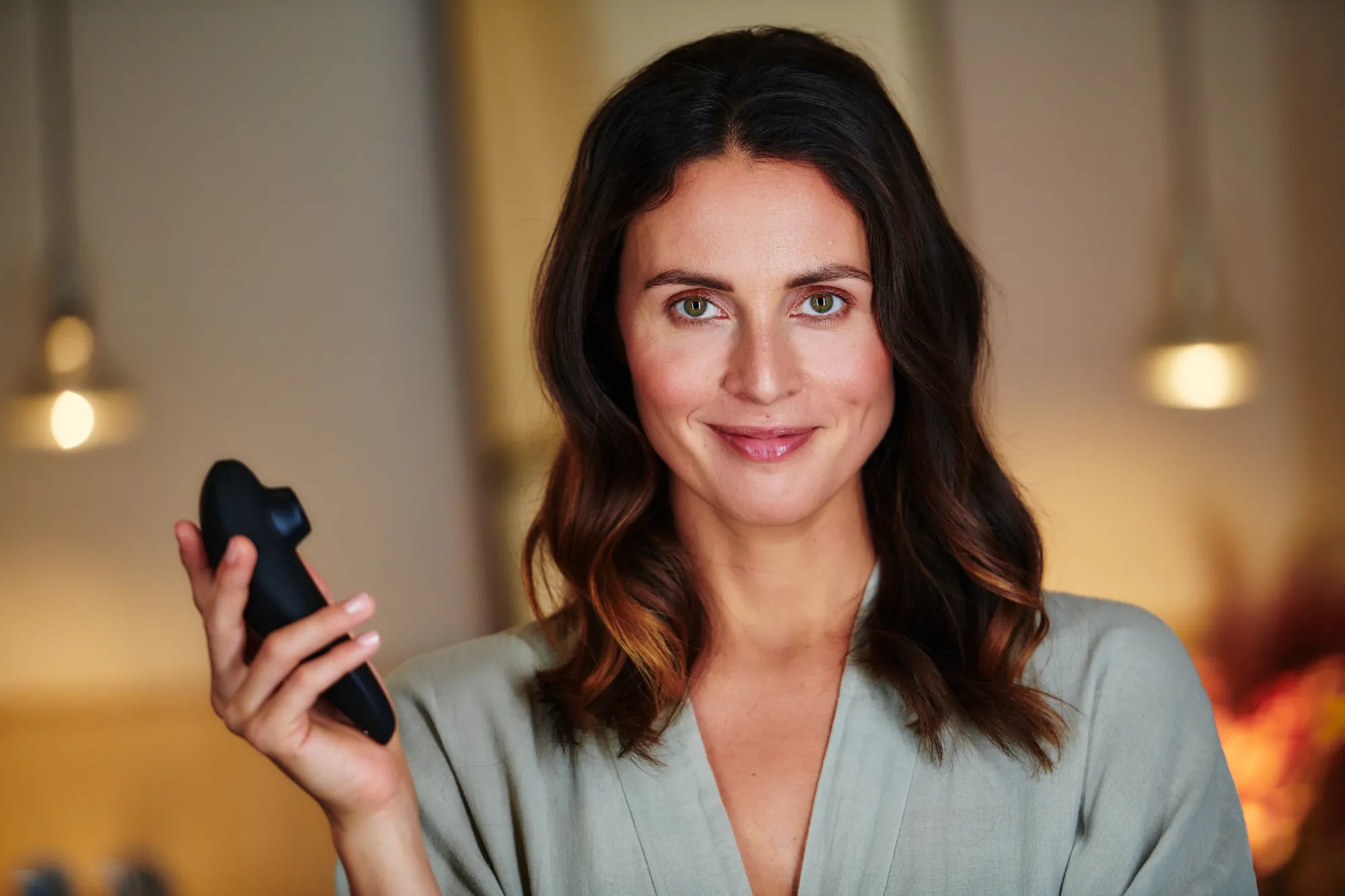 Kvinde i badekåbe smiler roligt og holder en Womanizer Classic 2 i hånden. Et elegant billede af sanselig selvtillid og moderne nydelse, som repræsenterer Womanizer-serien hos Nevola.