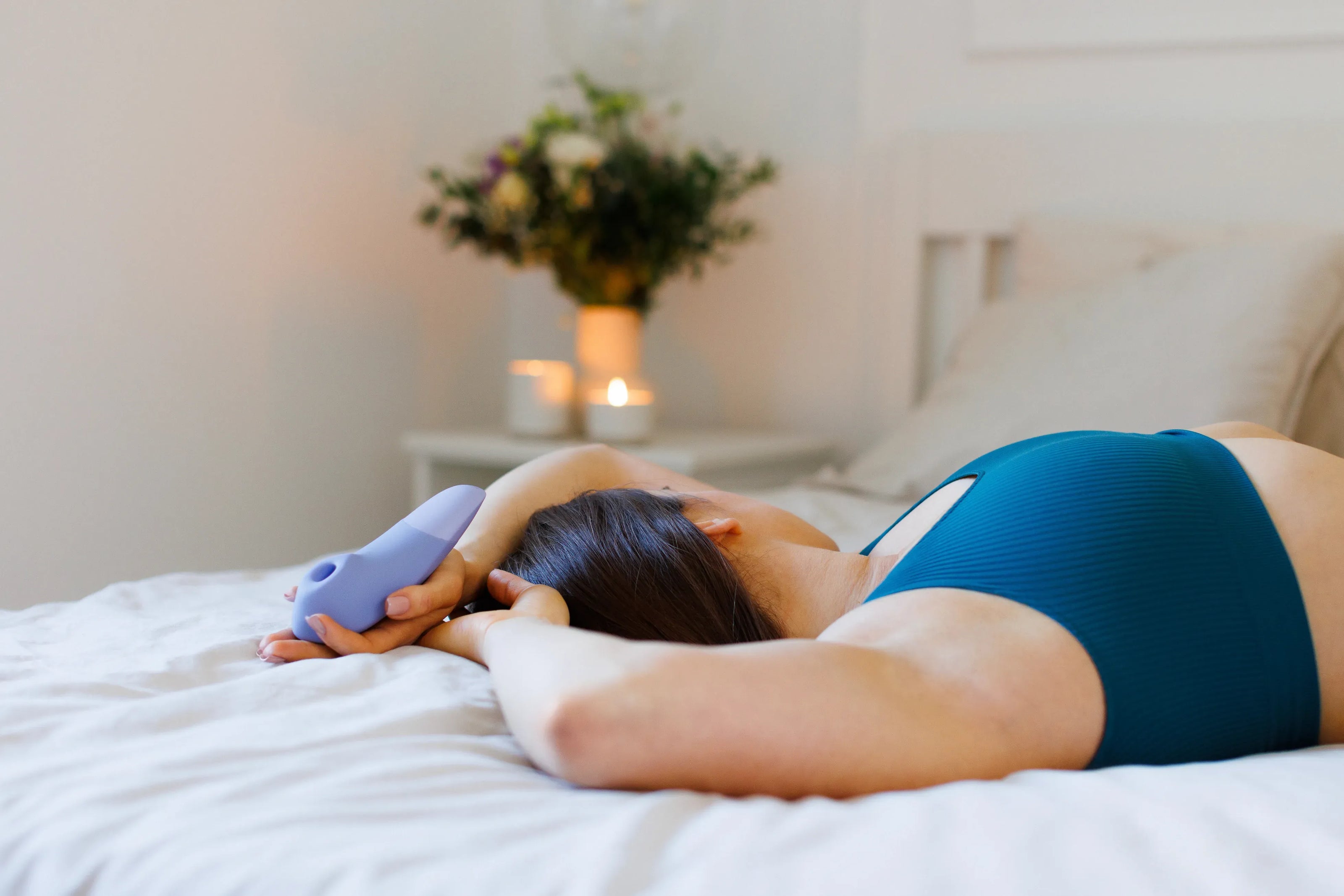 Kvinde ligger afslappet på sengen med Womanizer Enhance vibrator i lilla i hånden, et sensuelt sexlegetøj designet som intimprodukt til moderne wellness, tryg selvforkælelse og stilfuld stimulering i hverdagen.