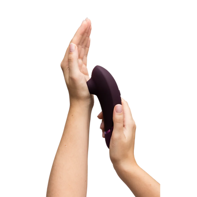 Womanizer Next i aubergine demonstreres mod håndfladen for at vise lufttryksteknologien. Et realistisk billede, der fremhæver blid stimulation og brugervenlig form.