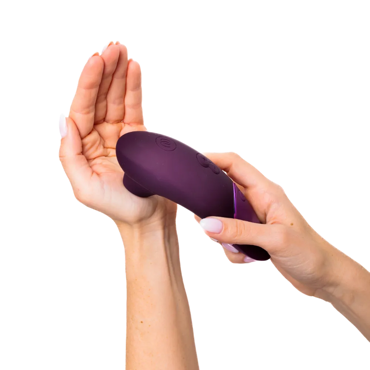 Womanizer Next i aubergine holdes ergonomisk i hånden. Fotoet viser den afrundede form og glatte silikoneoverflade, der giver en behagelig oplevelse.