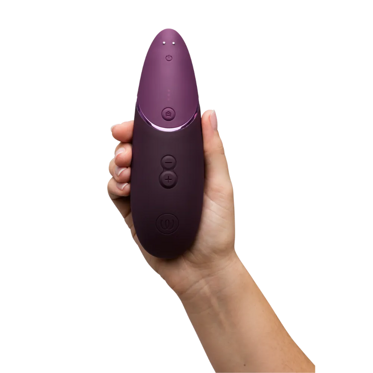 Womanizer Next i aubergine holdes oprejst i hånden. Et detaljeret foto, der viser knapper, topdesign og det glatte silikonefinish.