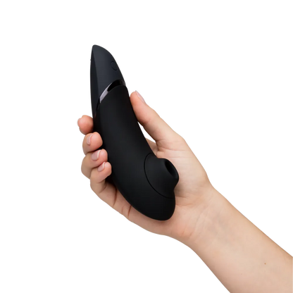 Womanizer Next i sort holdes i hånden. Et tydeligt produktbillede, der viser det ergonomiske design, knapplacering og komfortable greb.