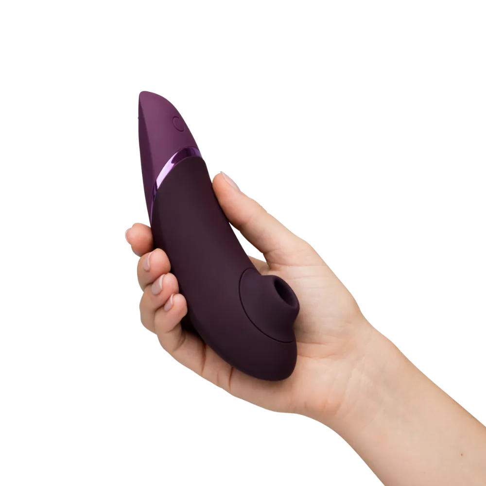 Womanizer Next i aubergine vises i hånden set forfra. Et elegant billede, der fremhæver luksuriøst design og intuitiv betjening.