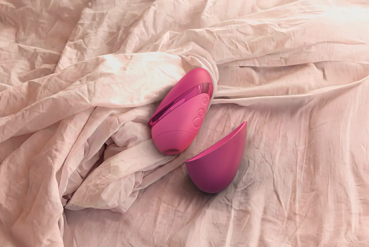 Womanizer Next Liberty i pink med aftageligt beskyttelsescover liggende på en seng